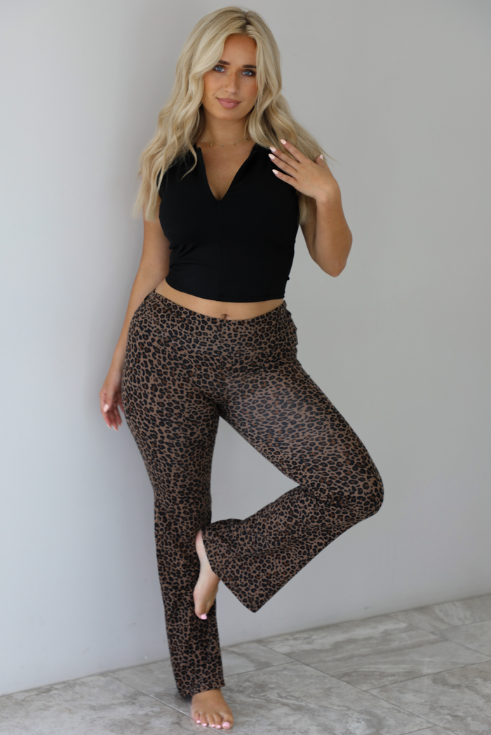 Woman wearing a black quarter zip sleeveless crop top with mid-rise leopard casual pants indoors against a white wall with white marble flooring. 