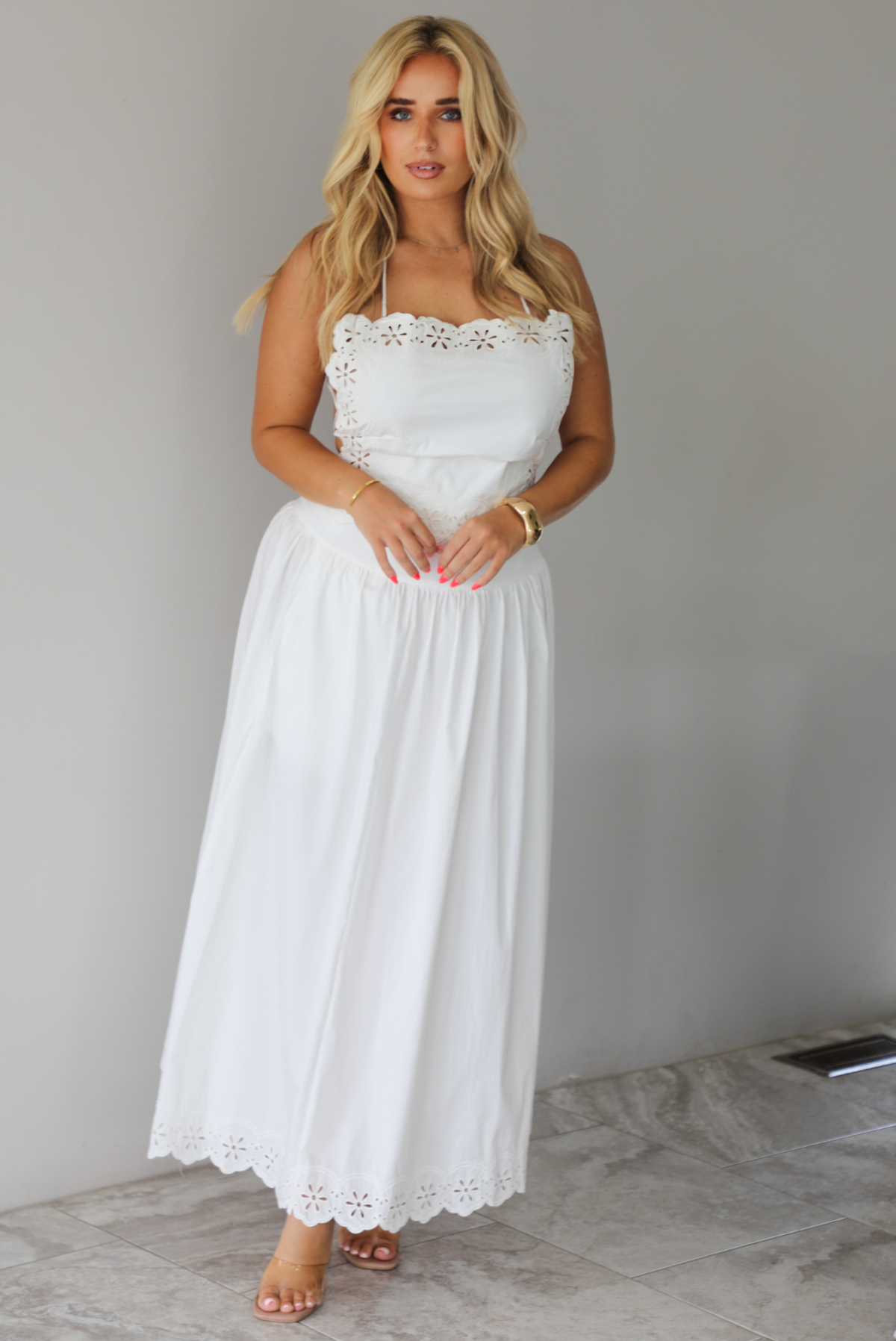 Woman wearing a two piece white set indoors against a white wall with white marble flooring. 