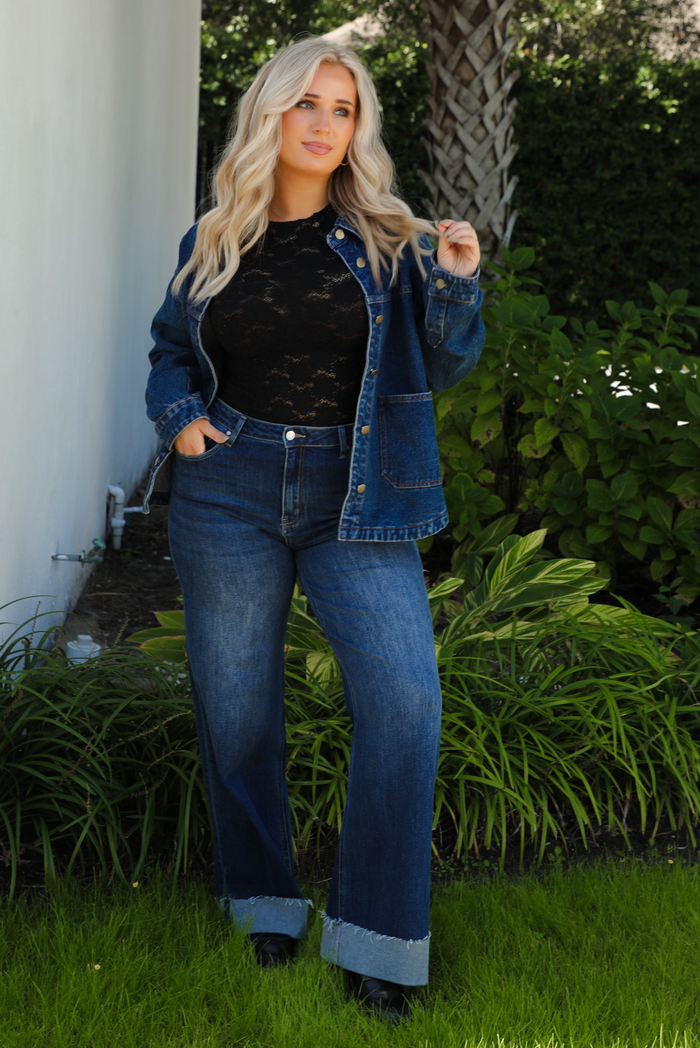 Woman model wearing a dark denim button up jacket with a black lace top,  and dark denim jeans outdoors. 