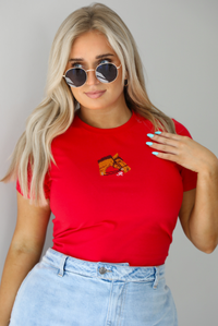 Woman wearing a red fitted baby tee with an embroidered horse graphic on the front. The top is paired with a high waisted, light-wash denim skort. The photo is taken indoors against a white wall.