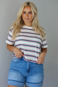 Woman wearing a striped, slightly cropped tee with light-wash denim shorts indoors against a white wall.