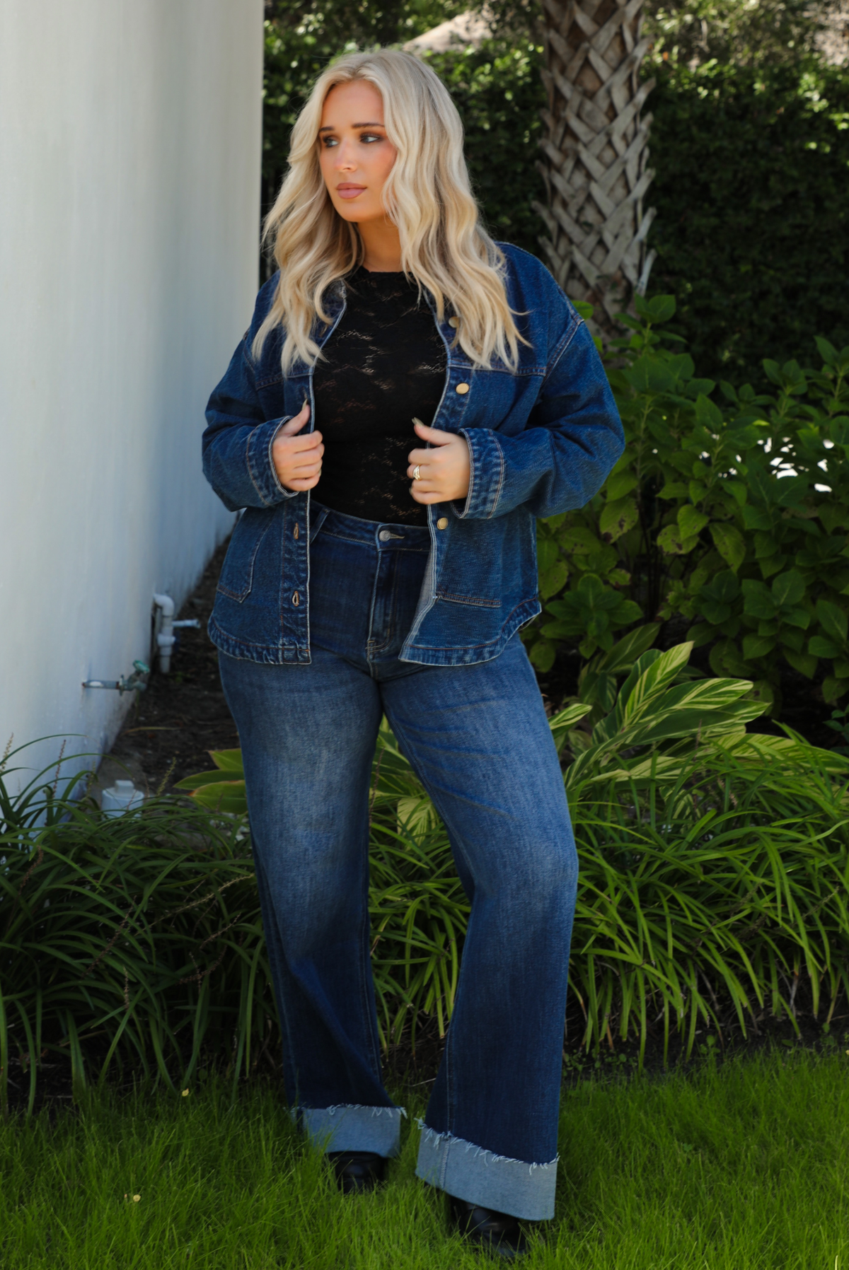 Woman model wearing a dark denim button up jacket with a black lace top,  and dark denim jeans outdoors. 