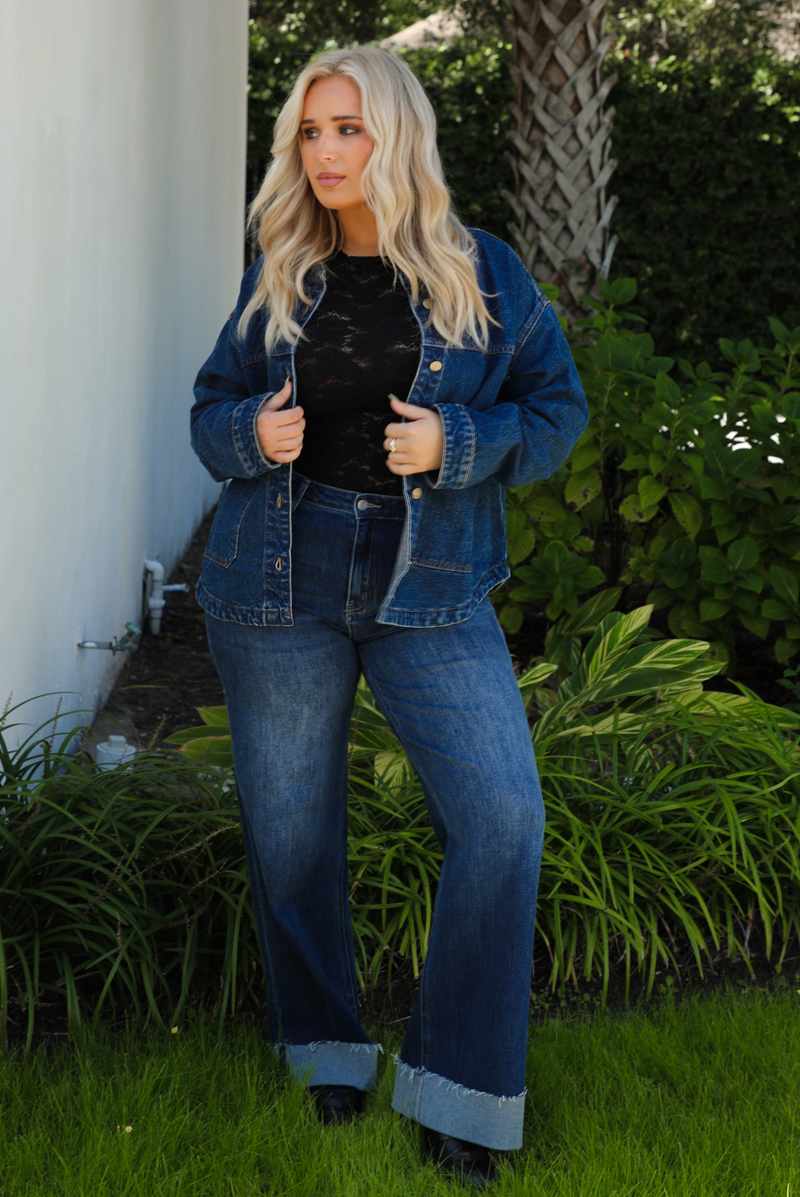 Woman model wearing a dark denim button up jacket with a black lace top,  and dark denim jeans outdoors. 
