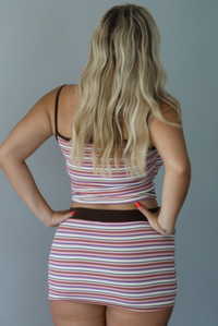 A woman posing outdoors in a pink, white, and brown striped set indoors against a white wall. The photo shows the back of the set. 