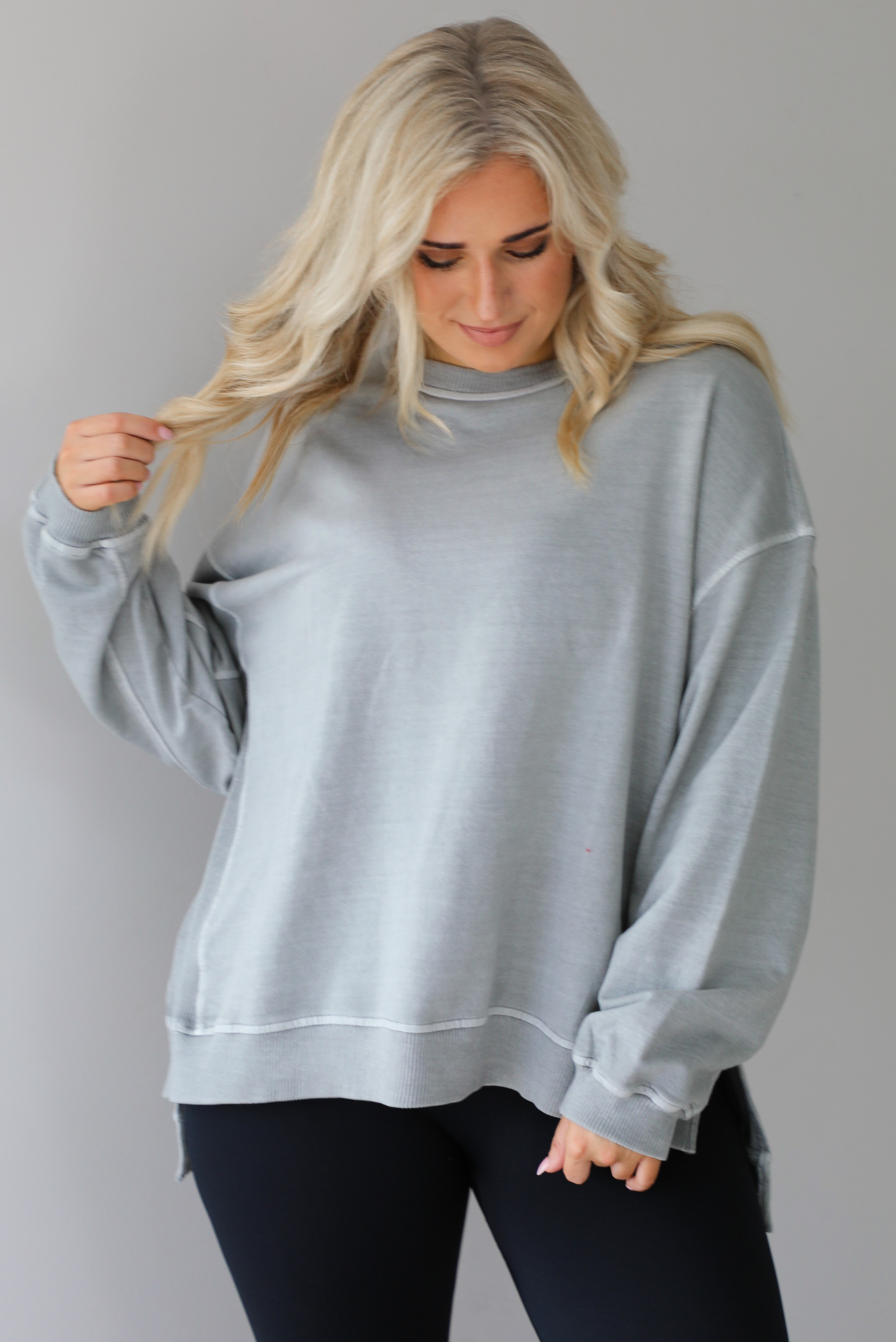 Woman wearing a grey oversized sweater with black leggings that have a slightly flared hem with split hem details in the front. The photo shows a closeup of the sweater and has a white background. 