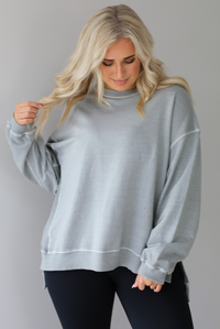 Woman wearing a grey oversized sweater with black leggings that have a slightly flared hem with split hem details in the front. The photo shows a closeup of the sweater and has a white background. 