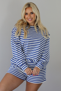 Woman wearing a navy and white striped two piece set featuring a long sleeved top and shorts indoors against a white wall.