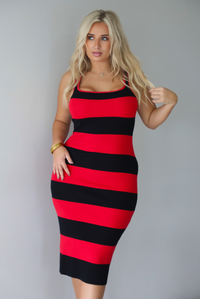 A woman wearing a red and black striped body-con midi dress standing indoors against a white wall.