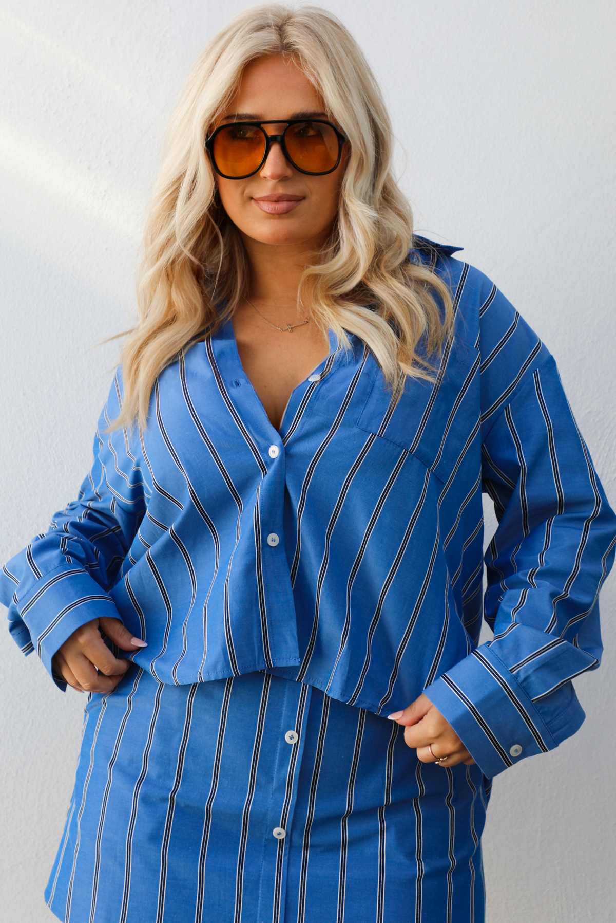 Woman wearing a blue striped set. with a white background. The set is a collared, button down cropped top with a skirt. 