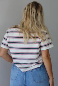 Woman wearing a striped, slightly cropped tee with light-wash denim shorts indoors against a white wall. The photo shows the back of the tee. 
