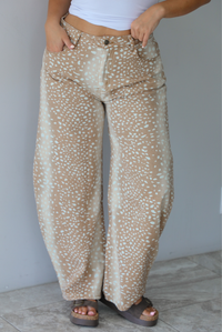 Person wearing sand and tan hombre design barrel denim jeans with a sand doe pattern with a mid-rise waistline, functional button and zipper closures in the front and functional front and back pockets indoors against a white wall with white marble flooring. 