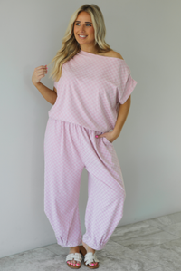 Woman wearing a pink checkered set featuring a slouchy top and pants. The photo is taken indoors against a white wall with white marble flooring.