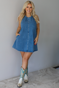 Woman wearing a denim blue dress indoors against a white wall with white marble flooring. 