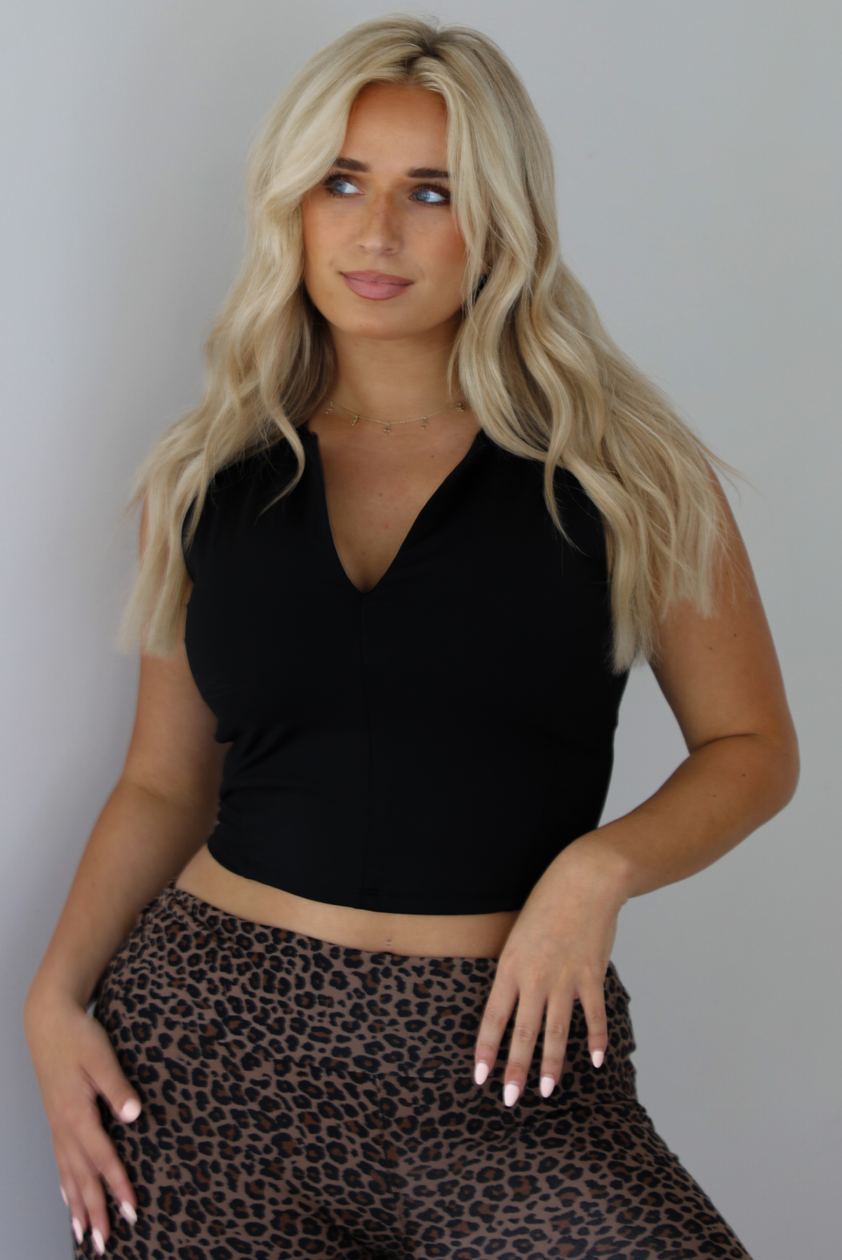 Woman wearing a black quarter zip sleeveless crop top with mid-rise leopard casual pants indoors against a white wall. The photo shows a closeup of the top. 