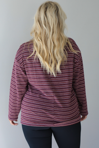A woman shown from behind wearing a burgundy striped long sleeved top paired with black leggings, standing indoors against a white wall. 