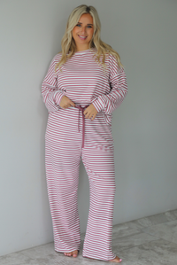 A woman wearing a matching two piece set featuring a long sleeved top and high waisted wide leg pants with a berry and white striped pattern throughout, standing indoors against a white wall with white marble flooring. 