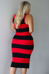 A woman shown from behind wearing a red and black striped body-con midi dress standing indoors against a white wall.