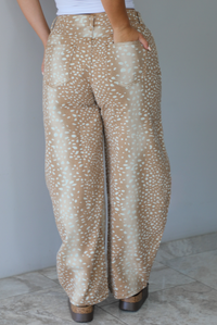 Person wearing sand and tan hombre design barrel denim jeans with a sand doe pattern with a mid-rise waistline, functional button and zipper closures in the front and functional front and back pockets indoors against a white wall with white marble flooring.  The photo shows the back of the pants. 