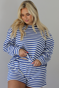 Woman wearing a navy and white striped two piece set featuring a long sleeved top and shorts indoors against a white wall.