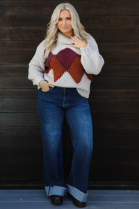 Woman model wearing a chunky knit turtle neck sweater with dark denim jeans outdoors in front of a dark wood door. 