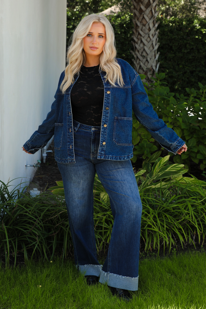 Woman model wearing a dark denim button up jacket with a black lace top,  and dark denim jeans outdoors. 