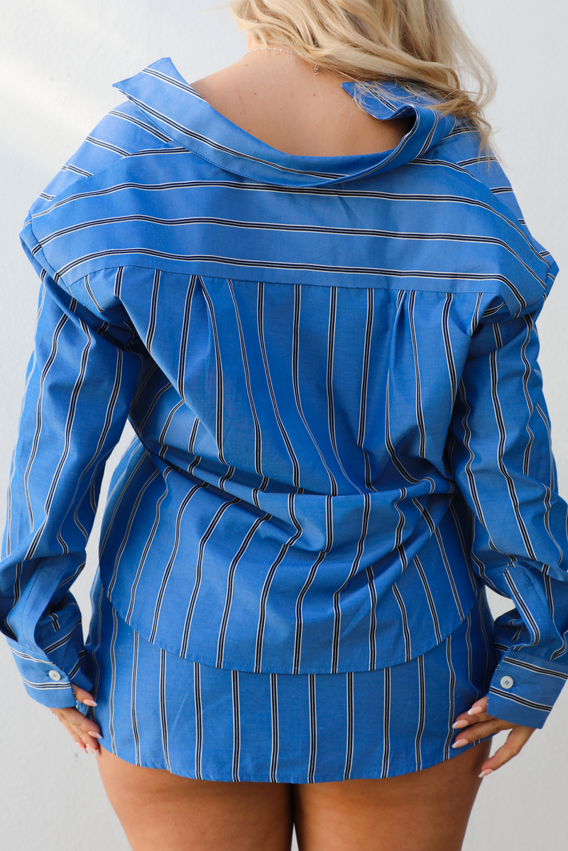 The back of a woman model wearing a blue striped set. with a white background. The set is a collared, button down cropped top with a skirt. 