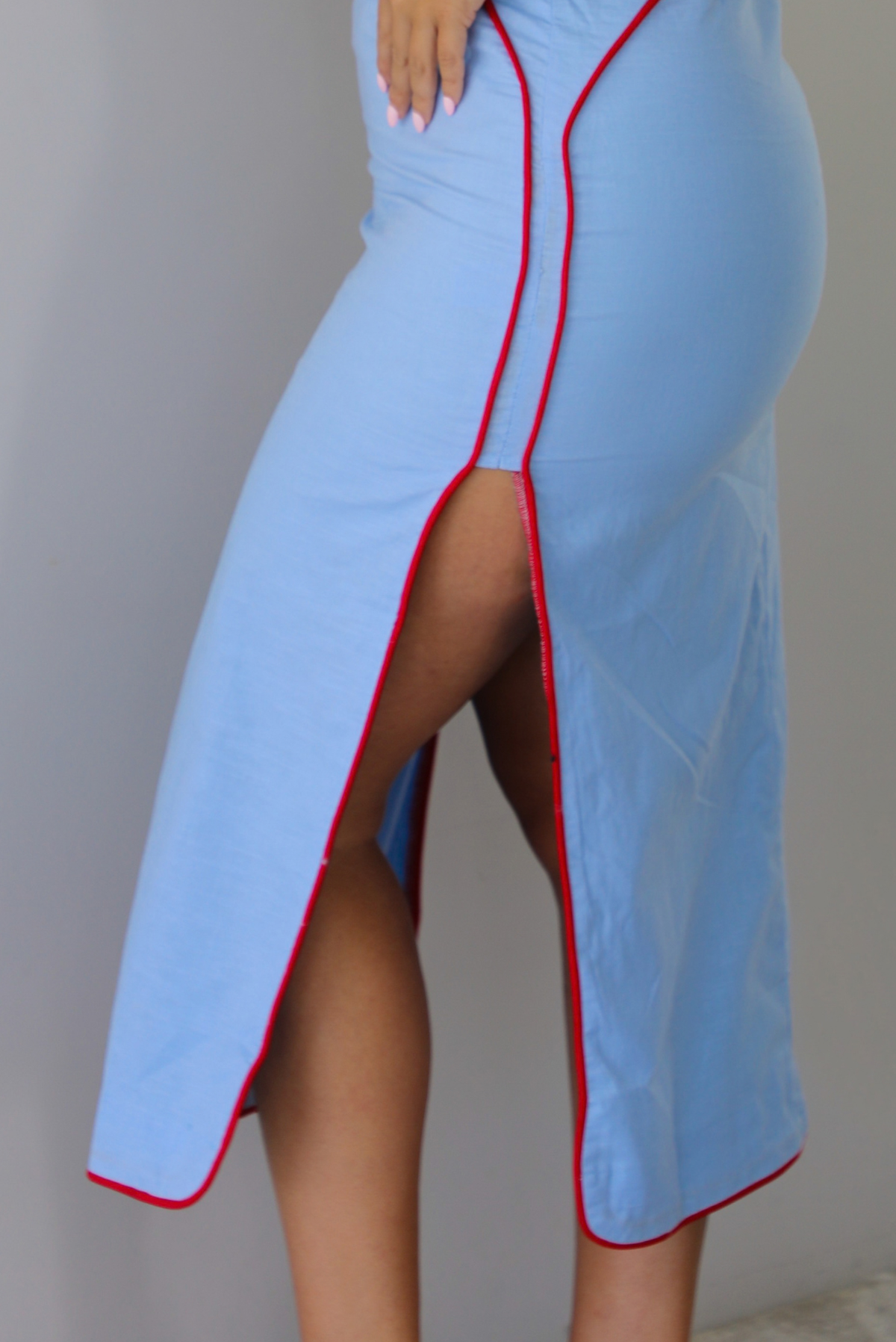 A blonde woman modeling a light blue halter midi dress with red trim, shown closeup and to the side, focused on the split hem detail.