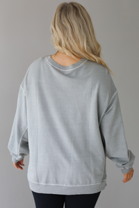 Woman wearing a grey oversized sweater with black leggings that have a slightly flared hem with split hem details in the front. The photo shows a closeup of the back of the sweater and has a white background. 