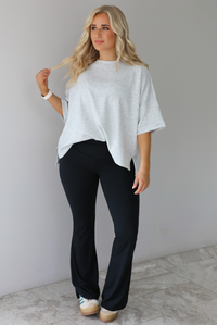 Woman wearing an oversized heather grey box tee with black leggings that flare slightly at the hems. The photo is taken indoors against a white wall with white marble flooring. 