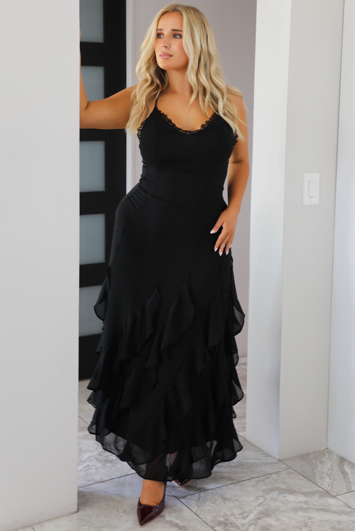 Woman wearing a black evening gown that has a flowy, ruffled skirt. The photo is taken inside a modern white and black  home. 