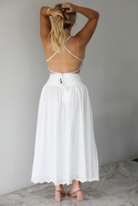 Woman wearing a two piece white set indoors against a white wall with white marble flooring. The photo shows the back of the set, which has an open back on the top. 