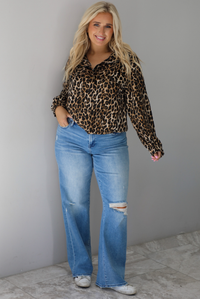A woman wearing a leopard collared jacket paired with a pair of medium wash distressed denim jeans, standing indoors against a white wall with white marble flooring. 