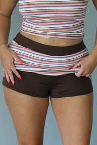 A woman posing outdoors in a pink, white, and brown striped set indoors against a white wall. The photo shows a close-up of the skirt, and the shorts liner underneath. 