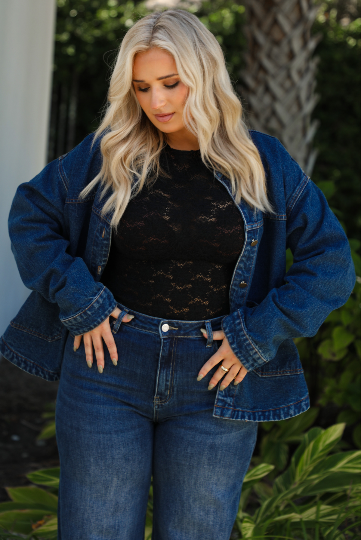 Close up of a woman model wearing a dark denim button up jacket with a black lace top,  and dark denim jeans outdoors. 