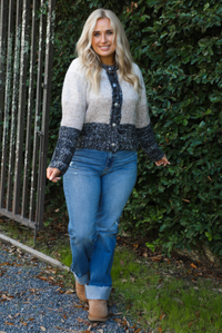 Colorblock designed cardigan with ivory, sand, oatmeal, and charcoal colors. The cardigan has functional button closures in the front with a relaxed fit. The cardigan is styled with medium wash denim. The photo is taken outdoors with greenery in the back. 