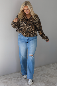 A woman wearing a leopard collared jacket paired with a pair of medium wash distressed denim jeans, standing indoors against a white wall with white marble flooring. 