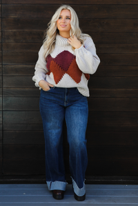 Woman model wearing a chunky knit turtle neck sweater with dark denim jeans outdoors in front of a dark wood door. 