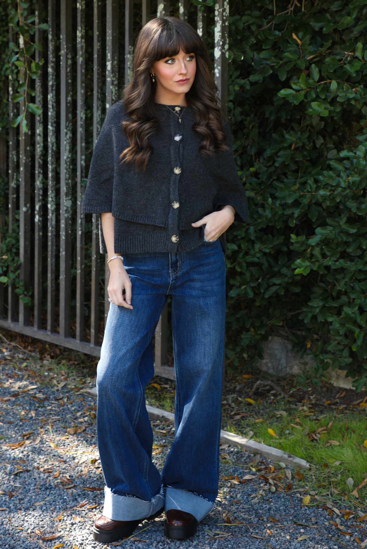 Woman model outdoors wearing a charcoal grey colored cape cardigan with functional button closures in the front and dark wash denim. 