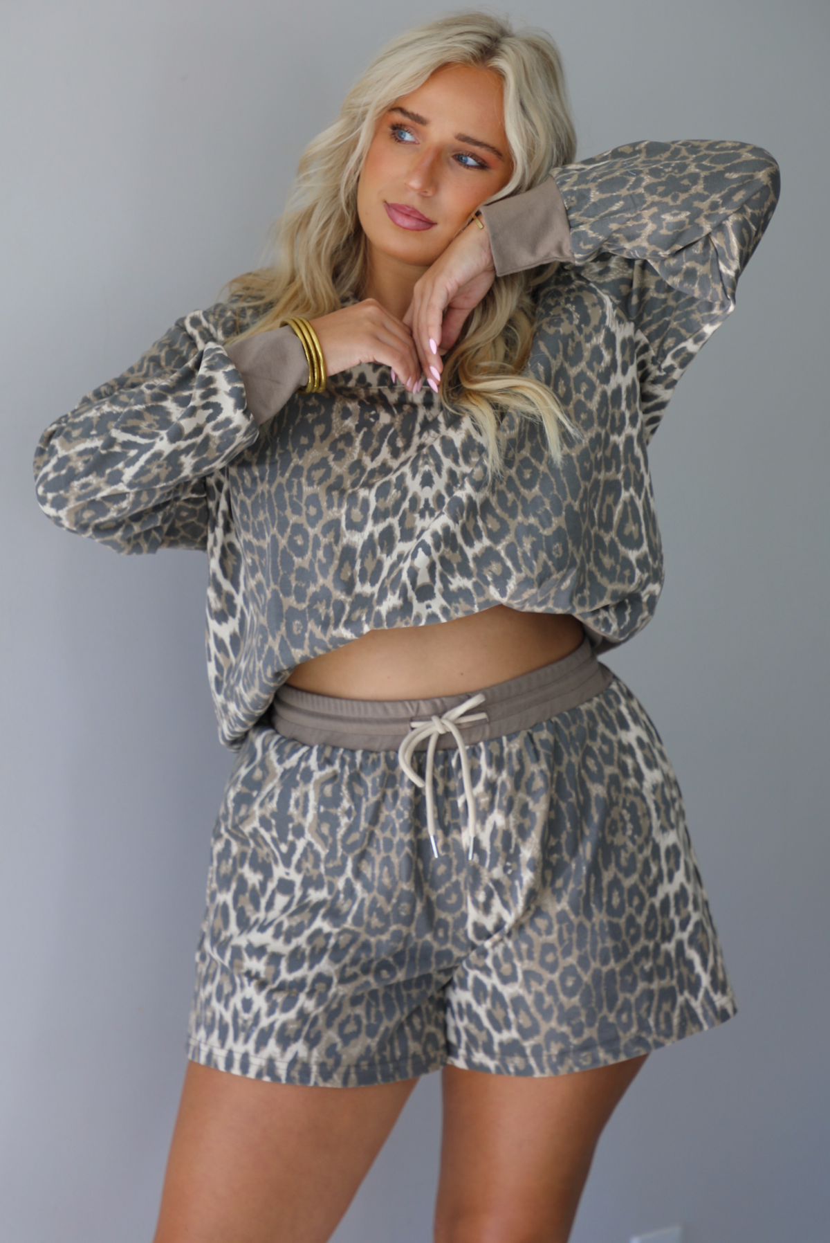 A woman modeling a matching leopard-print quarter-zip sweater that's bra-tucked to give it a cropped look and shorts set with gray drawstrings, standing indoors against a white wall.