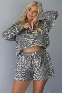 A woman modeling a matching leopard-print quarter-zip sweater that's bra-tucked to give it a cropped look and shorts set with gray drawstrings, standing indoors against a white wall.