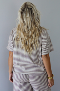 A woman shown from behind wearing a matching short-sleeve striped lounge set in beige and olive green, featuring a crewneck top and drawstring pants, posed against a solid white wall. 