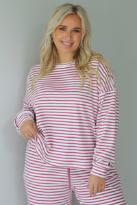 A woman wearing a matching two piece set featuring a long sleeved top and high waisted wide leg pants with a berry and white striped pattern throughout, standing indoors against a white wall. The photo shows the top untucked. 
