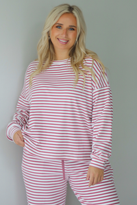 A woman wearing a matching two piece set featuring a long sleeved top and high waisted wide leg pants with a berry and white striped pattern throughout, standing indoors against a white wall. The photo shows the top untucked. 