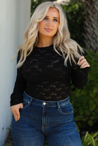Close up of model wearing black sheer lace top with a floral pattern with dark denim jeans outside.