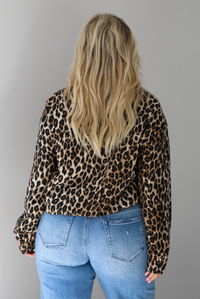 A woman shown from behind wearing a leopard collared jacket that has button and zipper closures in the front paired with a pair of medium wash distressed denim jeans, standing indoors against a white wall.