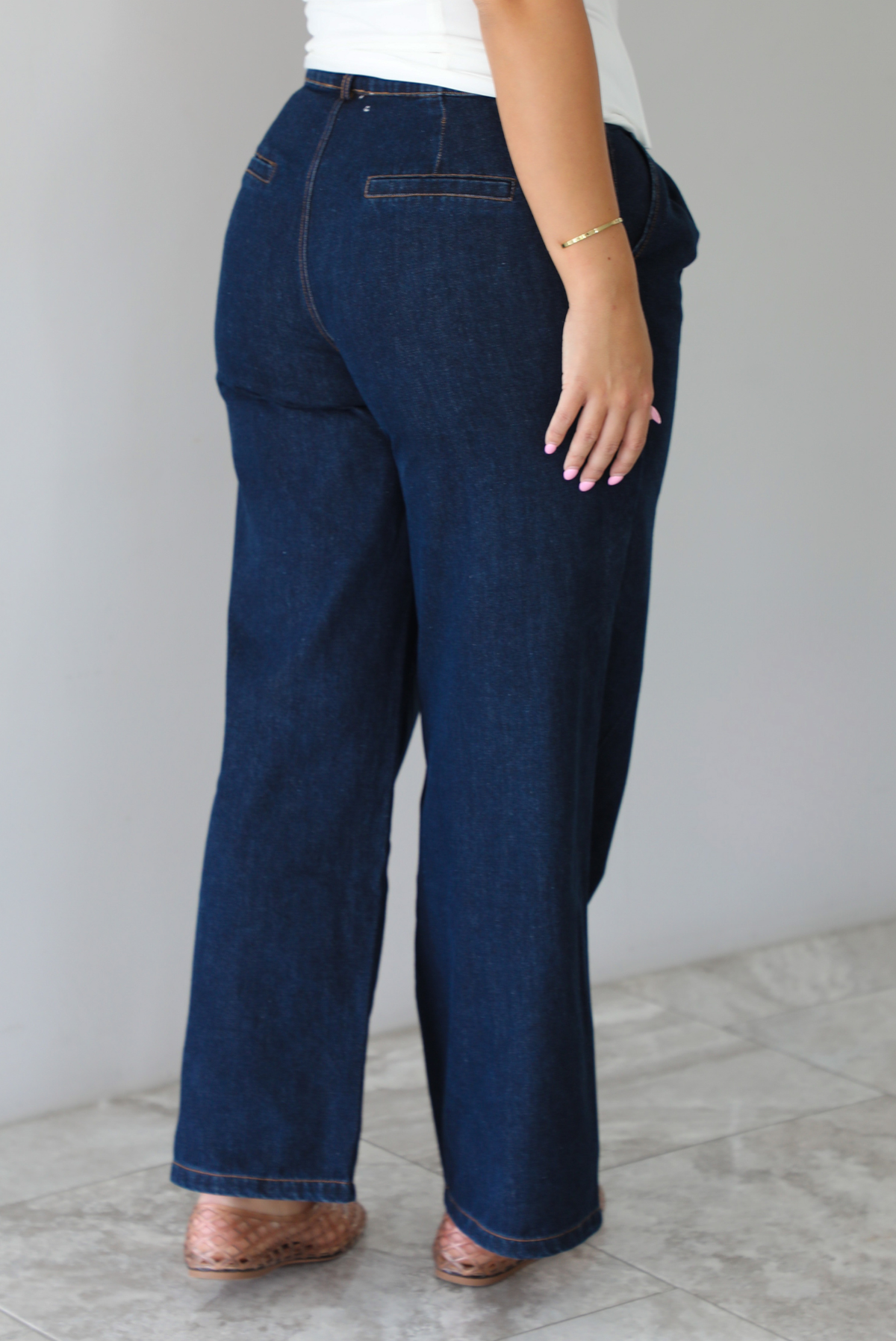 A person shown from behind wearing dark blue wide-leg denim jeans with a white lace-up drawstring waist top, standing indoors against a white wall with white marble flooring. 