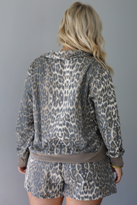 A woman shown from behind modeling a matching leopard-print quarter-zip sweater, untucked to show the full length, and shorts set with gray drawstrings, standing indoors against a white wall.