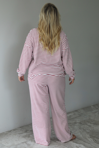 A woman shown from behind wearing a matching two piece set featuring a long sleeved top and high waisted wide leg pants with a berry and white striped pattern throughout, standing indoors against a white wall with white marble flooring. 