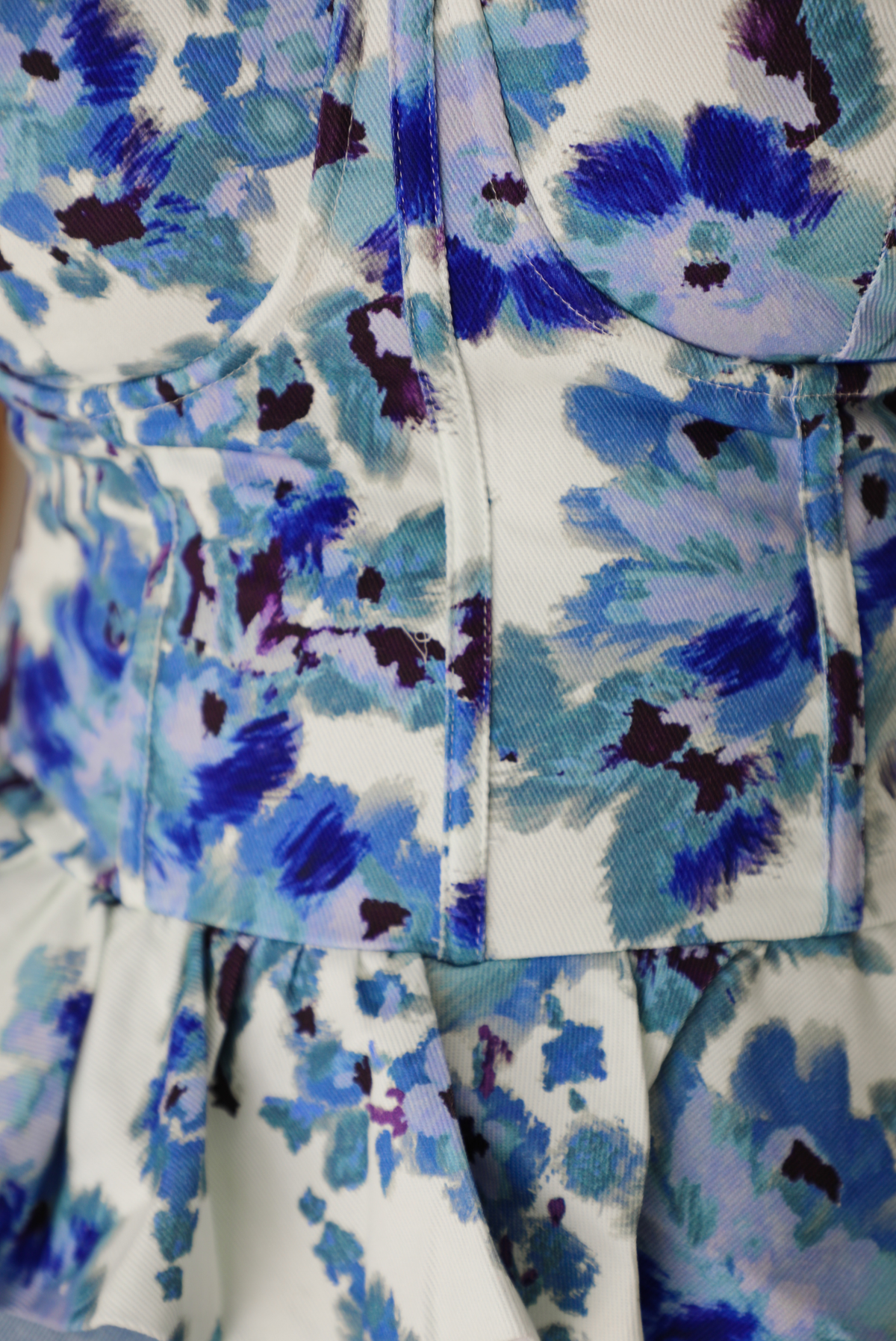 Woman wearing a blue and white strapless corset style top with a ruffled hem paired with light wash denim shorts. The photo shows a closeup of the fabric and pattern of the top, and you can also see the corset structuring. 
