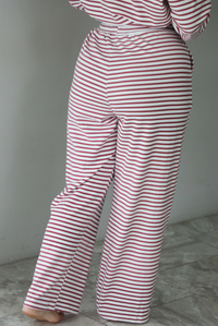 A woman shown from behind wearing a matching two piece set featuring a long sleeved top and high waisted wide leg pants with a berry and white striped pattern throughout, standing indoors against a white wall with white marble flooring. The photo shows a closeup of the back of the pants. 